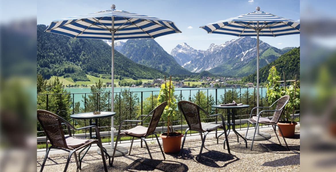 Outdoor restaurant dining area overlooking a lake, two round tables, and two striped market umbrellas providing shade