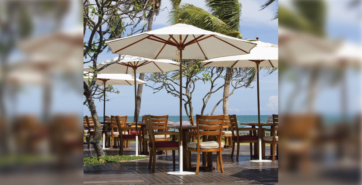 Outdoor restaurant dining area overlooking an ocean, with wood slat floors, wooden tables and chairs, with four Galtech International Designer Series 532TK54 patio umbrellas