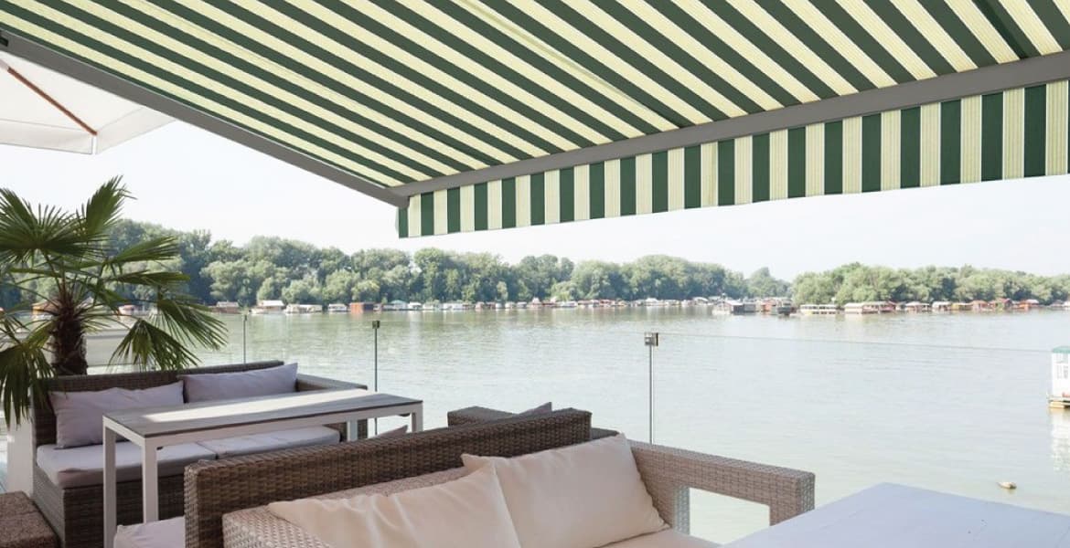 Outdoor casual dining space with loveseat seating, glass panel railing overlooking inlet to a lake or ocean with Advaning Luxury Series LUXURY premium UV sunshade canopy